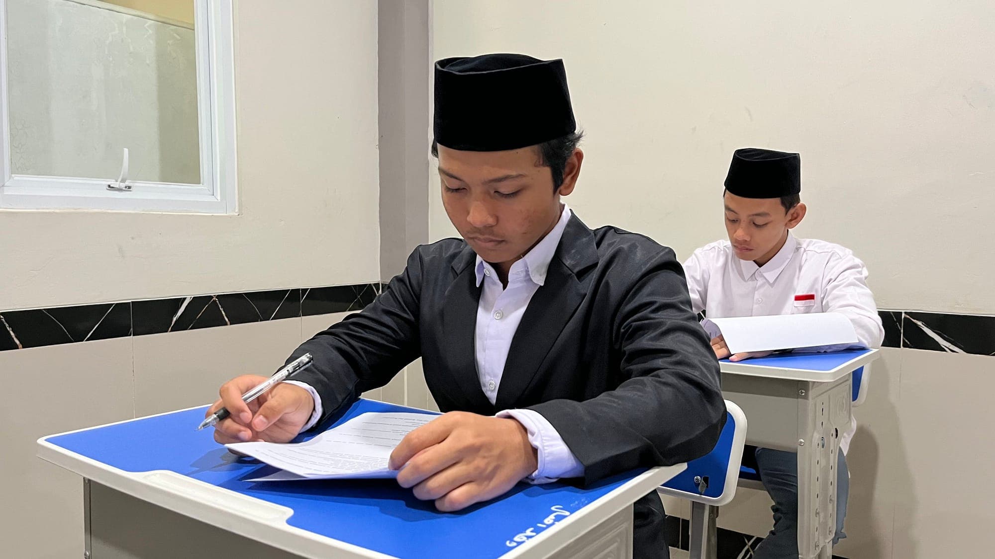 Santri MA Wadi Mubarak berjas dan berpeci hitam mengerjakan soal tertulis di ruang kelas