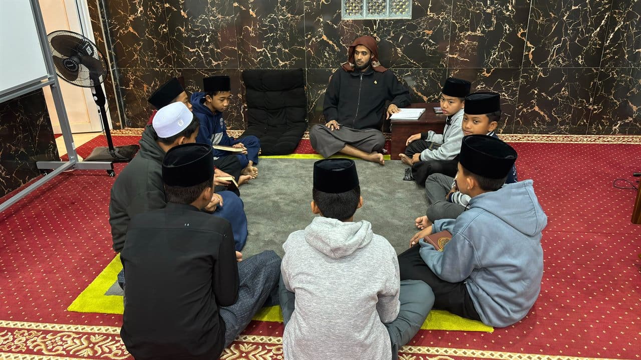 Halaqah setoran hafalan Program Kaderisasi Muhaffizh: pengampu menyimak delapan santri yang duduk melingkar di atas karpet masjid pondok