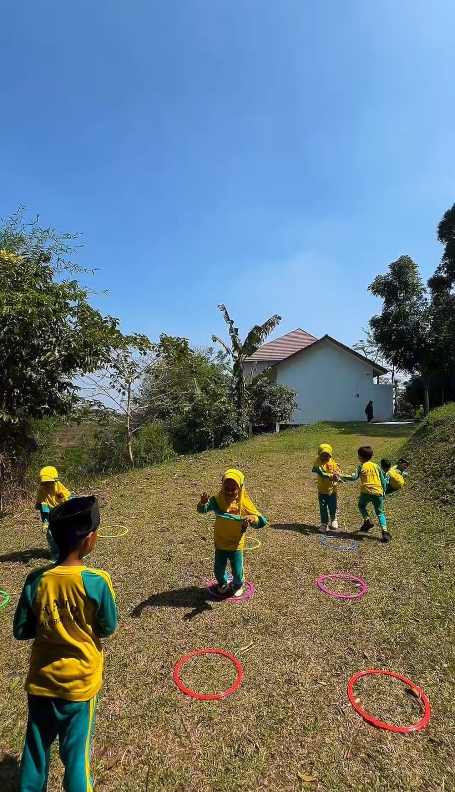 Anak-anak TAUD SAQU bermain lompat simpai di lapangan rumput di bawah langit cerah