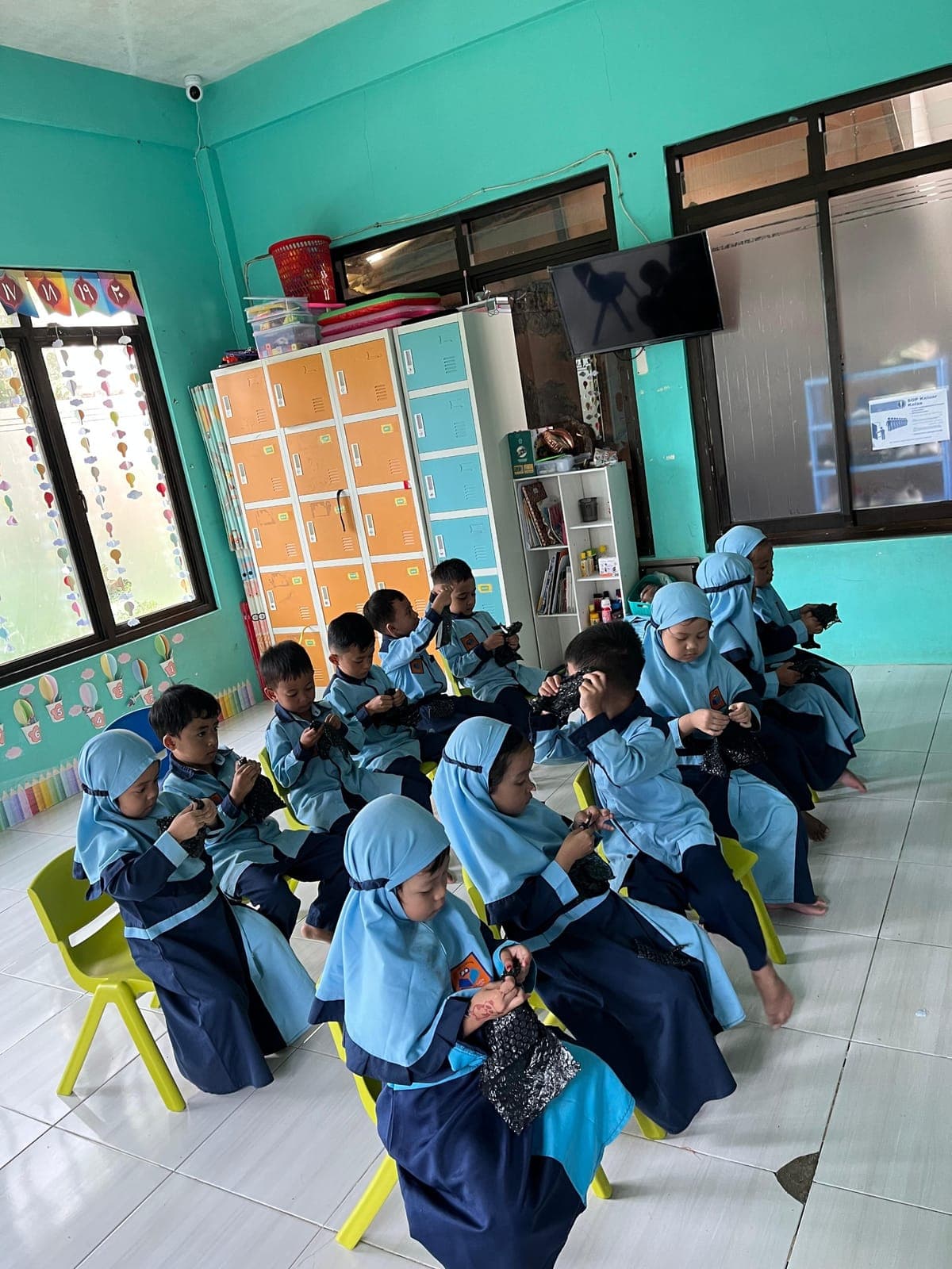 Anak-anak TAUD SAQU berseragam biru duduk di kursi kecil menekuni kegiatan di ruang kelas